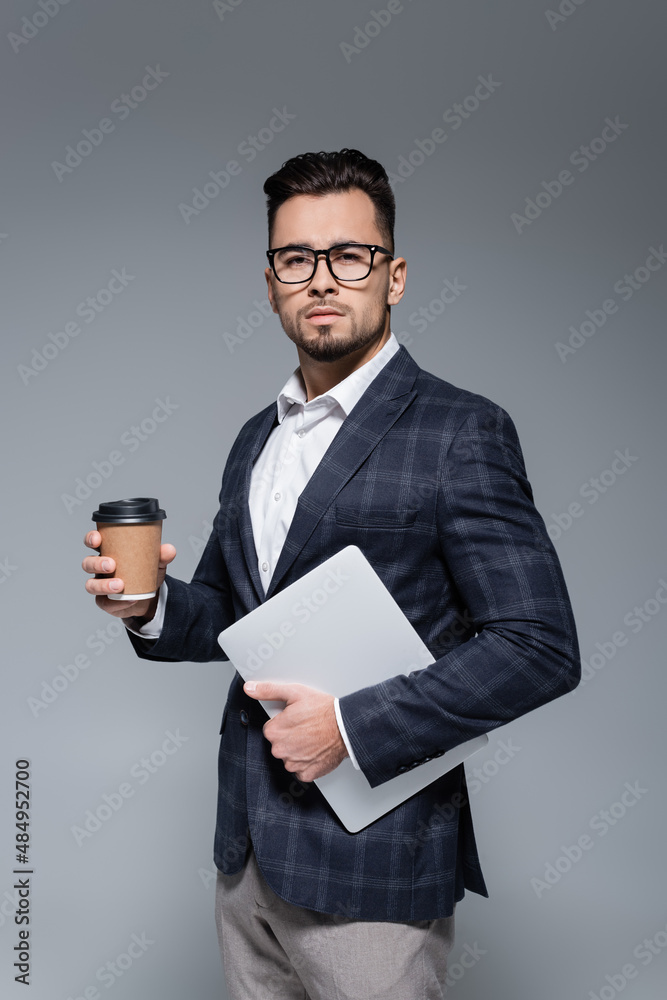 businessman in suit and glasses holding laptop and paper cup isolated on grey. businessman in suit and glasses holding laptop and paper cup isolated on grey.