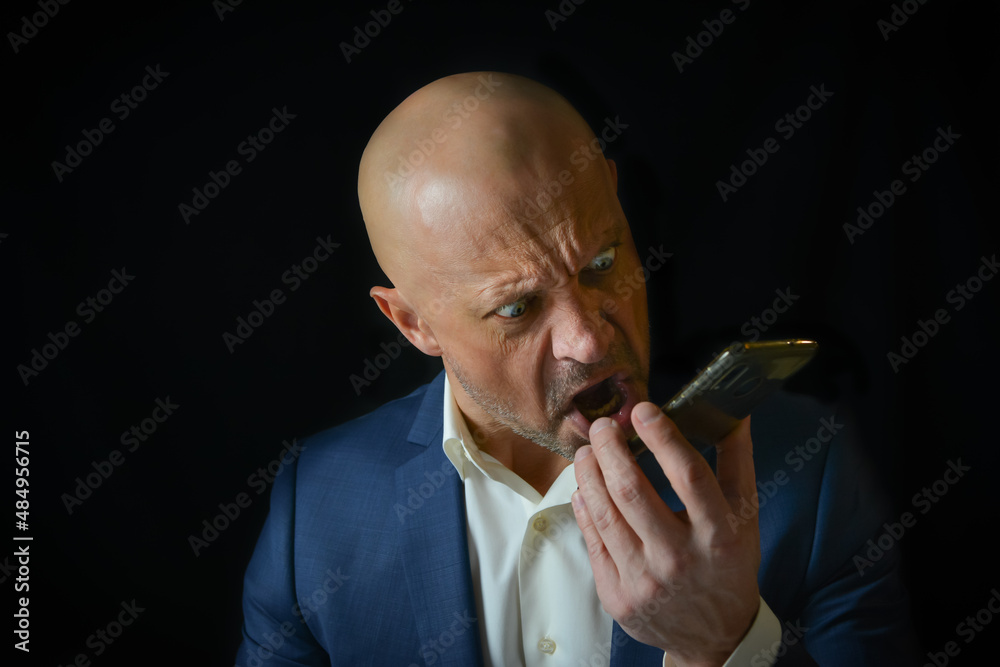 A man in a business suit emotionally swears on the phone. Enraged and angry boss screams into the telephone receiver. A man in a business suit emotionally swears on the phone. Enraged and angry boss screams into the telephone receiver.