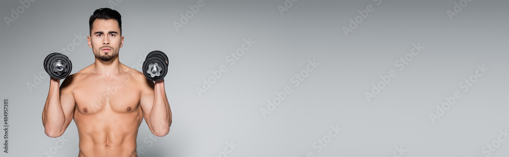 strong young sportsman working out with dumbbells on grey, banner. strong young sportsman working out with dumbbells on grey, banner.