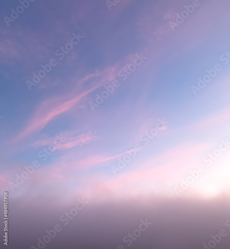Sunrise creates beautiful pink colors on the clouds above the grey morning fog.
