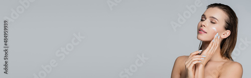 Fotografia young woman with closed eyes and cosmetic cream on face isolated on grey, banner