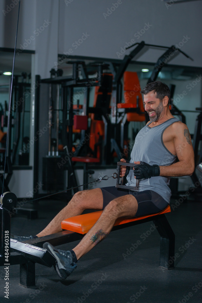 Fitness training in sport gym of active male with beard sitting and pulling heavy weight on exercise equipment Fitness training in sport gym of active male with beard sitting and pulling heavy weight on exercise equipment