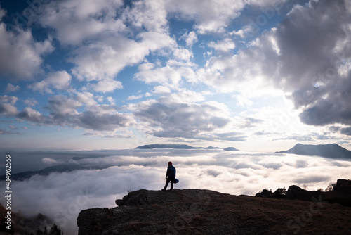 A person standing on the edge of the cliff over clouds