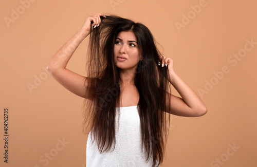 Frustrated armenian woman showing her damaged long locks, having bad hair day, upset over her messy hairdo photo