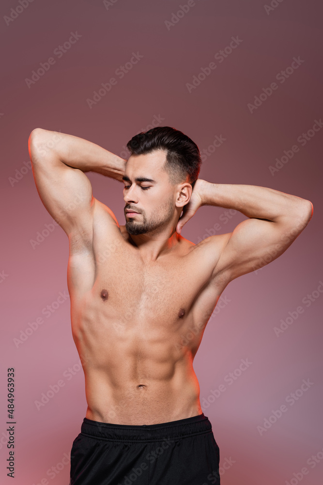 lighting on shirtless man with muscles posing on pink and grey.