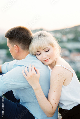 Woman hugs a man from behind with her head on his shoulder. Portrait