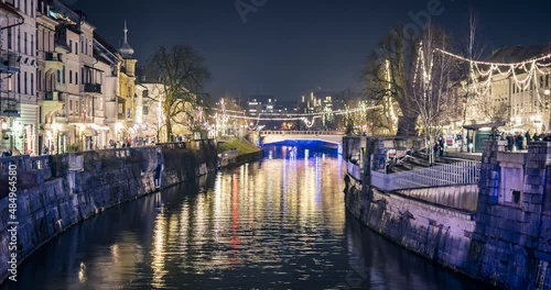 Night time lapse of tourist boats passing by on Ljubljanica river. Christmas and new year festive time in Ljubljana city, Slovenia. Lights decoration in downtown. Elevated view. Static shot