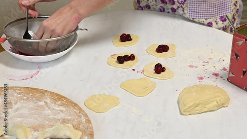 A woman puts cherries on the rolled dough. Cooking dumplings.