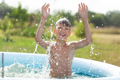 Cheerful child splashes in an inflatable pool on a sunny summer day in nature, selective focus on water splash.