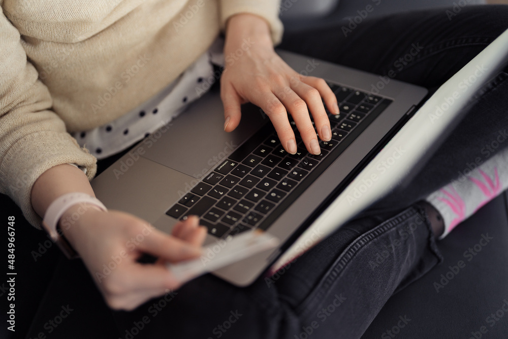 Online shopping using card and laptop. Woman handsusing technology to shop while sitting on a sofa indoors Online shopping using card and laptop. Woman handsusing technology to shop while sitting on a sofa indoors