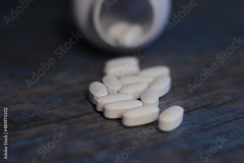 Pastillas blancas encima de una mesa de madera y de fondo un bote de pastillas