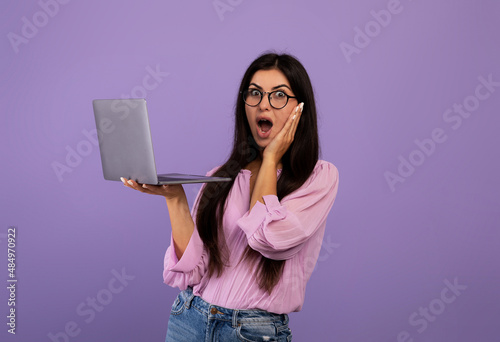 Shocked armenian woman holding laptop, having problems with computer, suffering bad internet connection