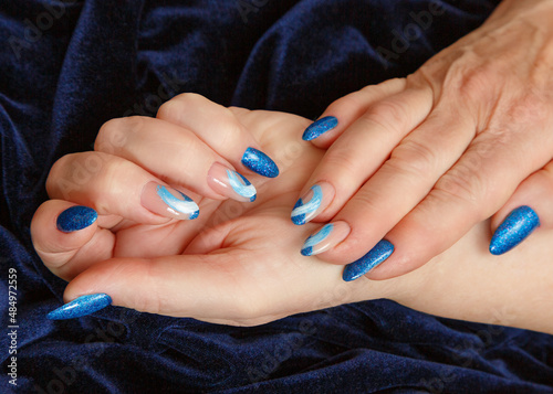 Female hands with a multicolored manicure on dark blue background closeup
