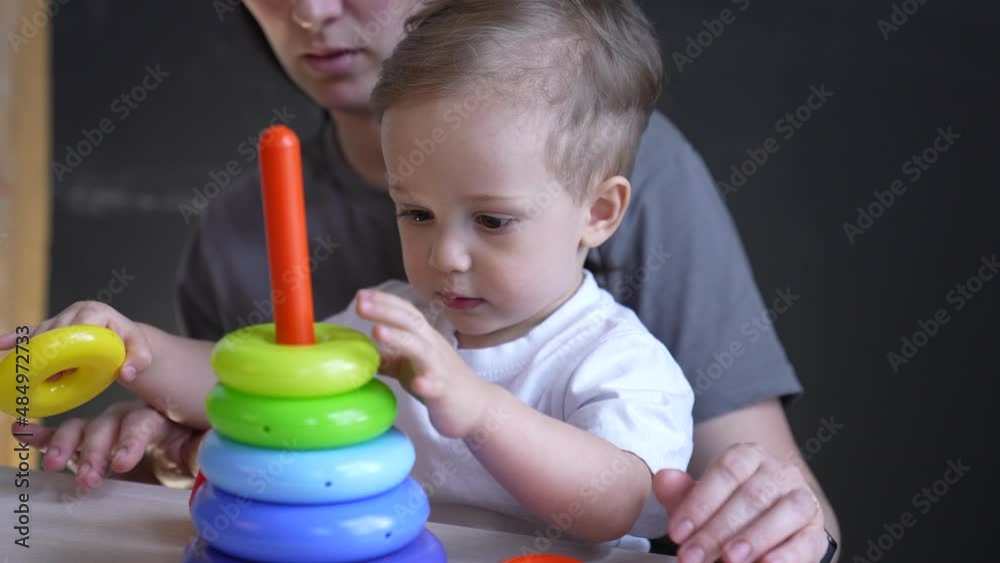baby collects toy pyramid. mom plays with her son at home happy family. development of fine motor skills in newborn child. happy family mom preschool and baby play pyramid toy. kindergarten education baby collects toy pyramid. mom plays with her son at home happy family. development of fine motor skills in newborn child. happy family mom preschool and baby play pyramid toy. kindergarten education