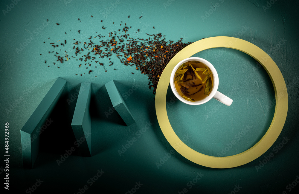 White cup of tea overhead image on teal background with triangle elements, moody shadows.  Green circle.