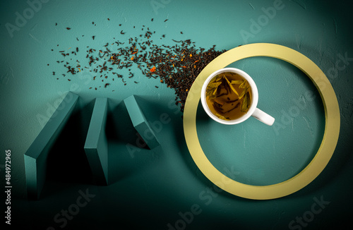 White cup of tea overhead image on teal background with triangle elements, moody shadows. Green circle.