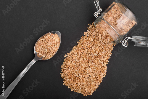 dried garlic spills out of a jar and lies in a spoon on a black background with copy spase