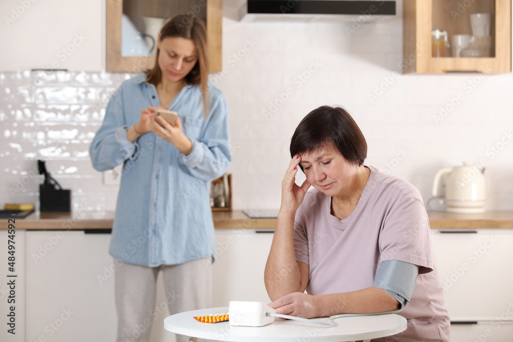 worried young woman calling doctor for her senior mother at home. sick senior woman with medication sitting at the table and measuring blood pressure. medicine and health concept worried young woman calling doctor for her senior mother at home. sick senior woman with medication sitting at the table and measuring blood pressure. medicine and health concept