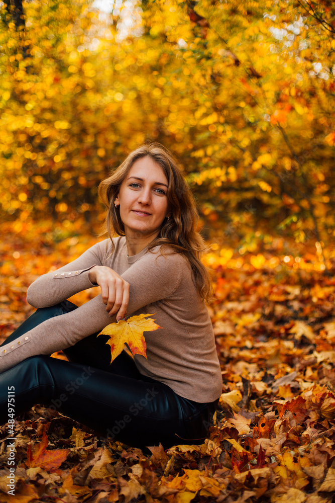 Beautiful girl is sitting on yellow leaves in the park. Attractive woman wearing beige sweater and black pants is walking in autumn park. Bright, warm sunny autumn day with yellow background.
Beautiful girl is sitting on yellow leaves in the park. Attractive woman wearing beige sweater and black pants is walking in autumn park. Bright, warm sunny autumn day with yellow background.