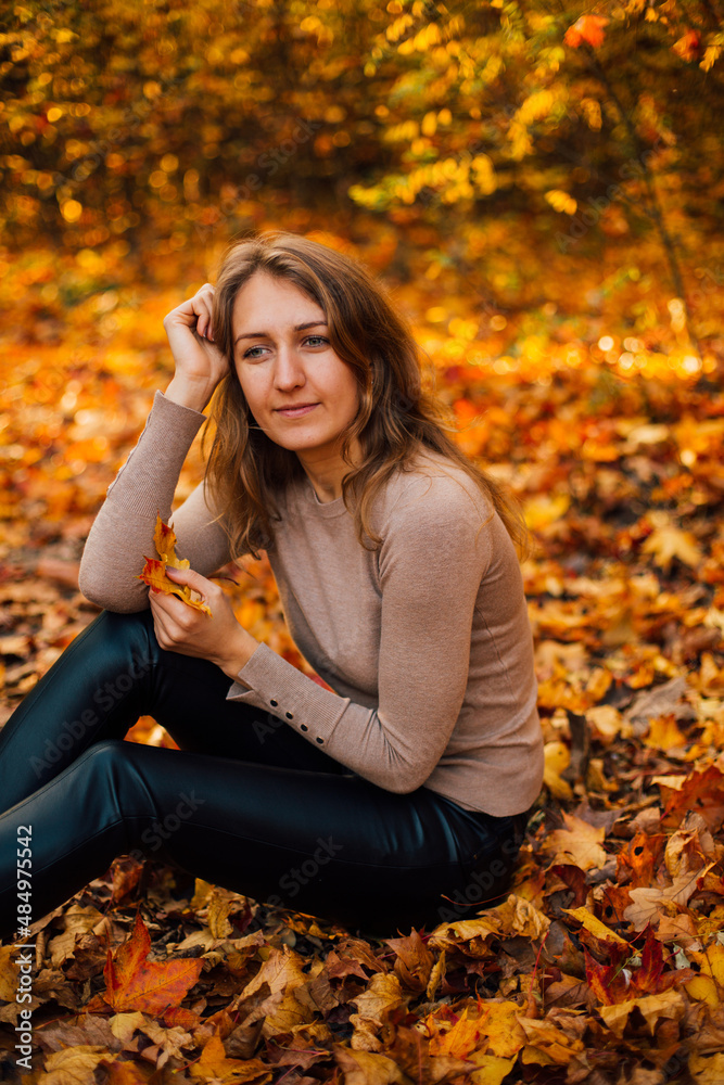 Beautiful girl is sitting on yellow leaves in the park. Attractive woman wearing beige sweater and black pants is walking in autumn park. Bright, warm sunny autumn day with yellow background.
Beautiful girl is sitting on yellow leaves in the park. Attractive woman wearing beige sweater and black pants is walking in autumn park. Bright, warm sunny autumn day with yellow background.