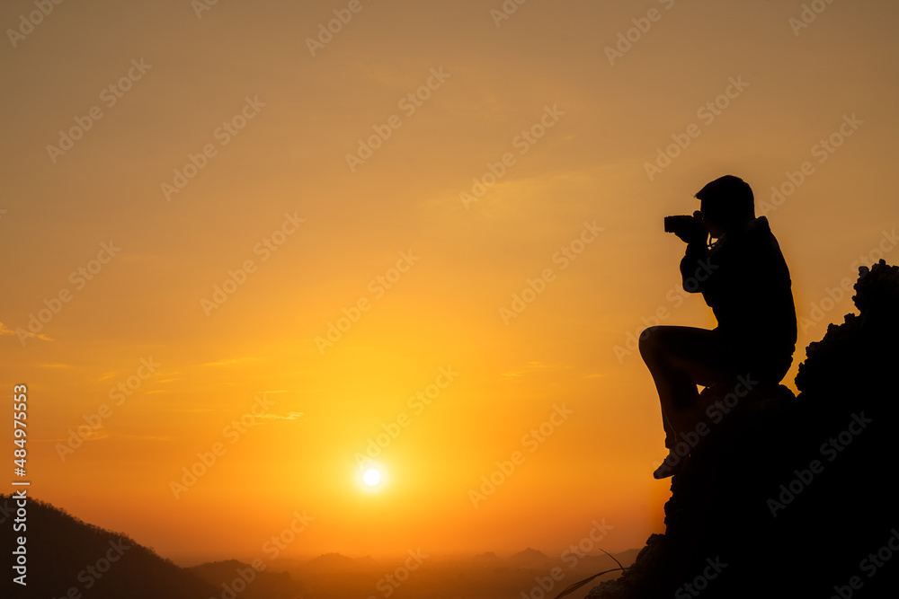 Fototapeta premium Silhuette of photographer traveler taking photo of beautiful sunset from top of the mountain