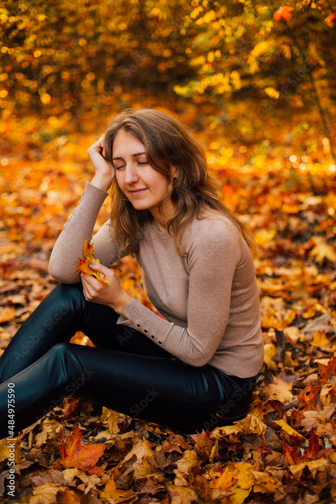 Beautiful girl is sitting on yellow leaves in the park. Attractive woman wearing beige sweater and black pants is walking in autumn park. Bright, warm sunny autumn day with yellow background.
Beautiful girl is sitting on yellow leaves in the park. Attractive woman wearing beige sweater and black pants is walking in autumn park. Bright, warm sunny autumn day with yellow background.