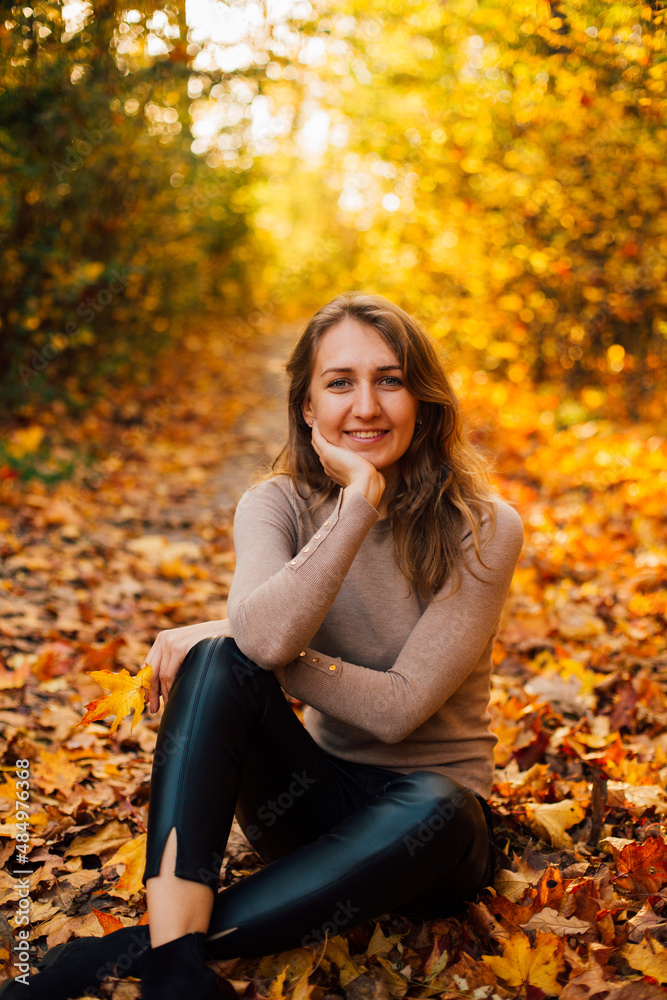 Beautiful girl is sitting on yellow leaves in the park. Attractive woman wearing beige sweater and black pants is walking in autumn park. Bright, warm sunny autumn day with yellow background.
Beautiful girl is sitting on yellow leaves in the park. Attractive woman wearing beige sweater and black pants is walking in autumn park. Bright, warm sunny autumn day with yellow background.