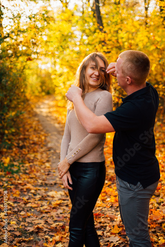 Young couple is having a walk in the sunny autumn park  forest. Happy man and his woman are hugging . Fallen yellow leaves  brith warm autumn weather. Autumn love story in park 