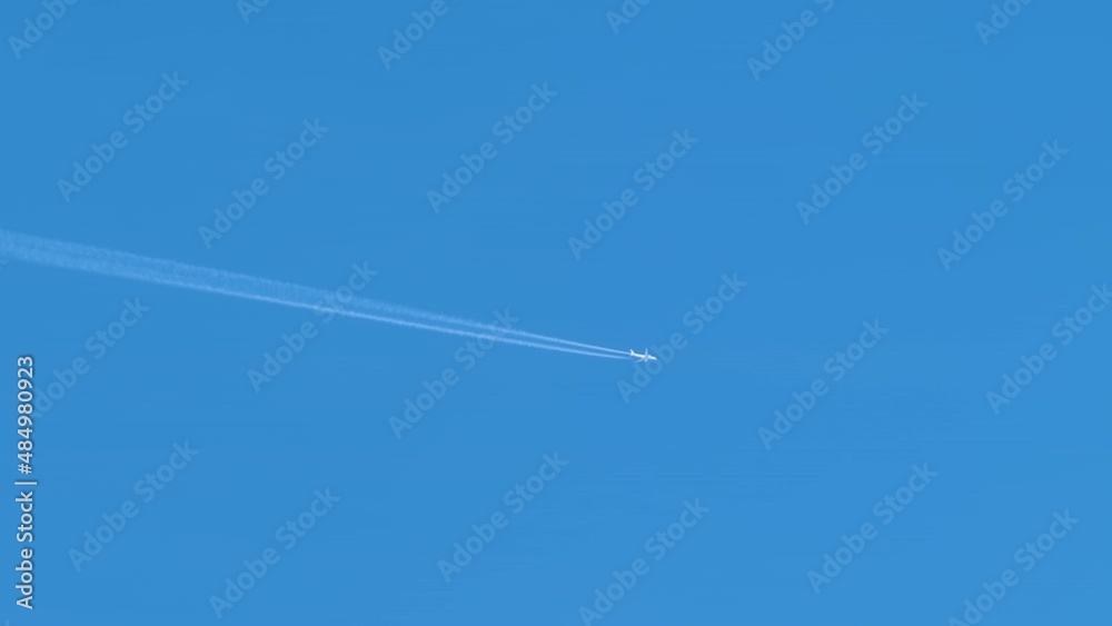 Distant passenger jet plane flying on high altitude on clear blue sky leaving white smoke trace of contrail behind. Air transportation concept Distant passenger jet plane flying on high altitude on clear blue sky leaving white smoke trace of contrail behind. Air transportation concept