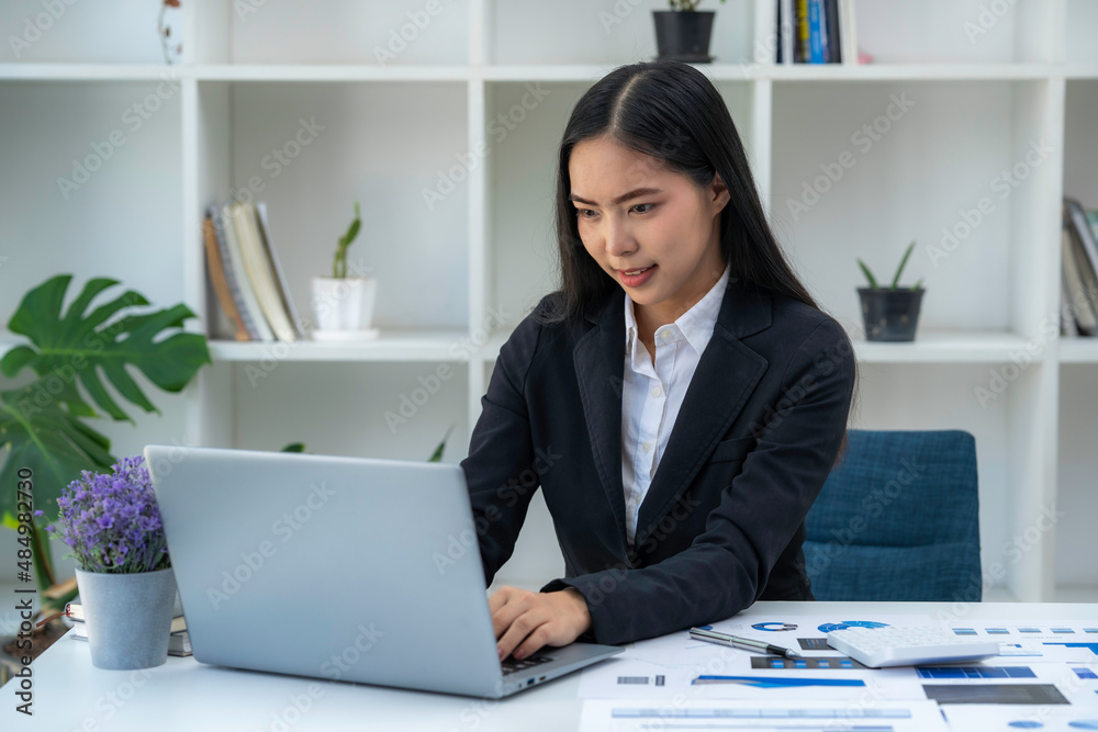 Asian businesswoman working on tablet and taking notes, accountant use a computer laptop at work in the office.