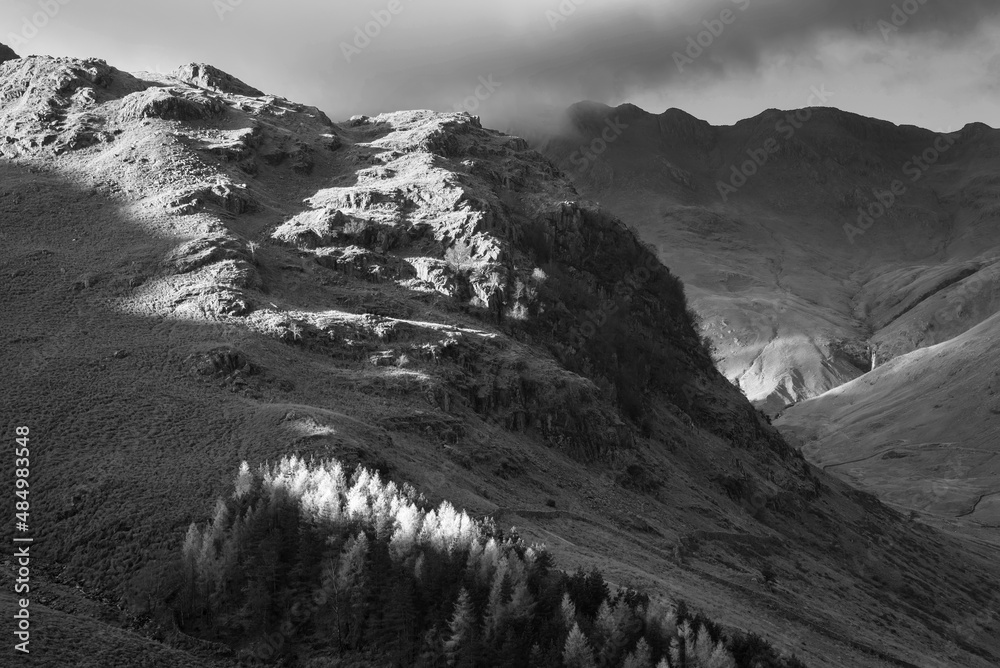 Black and white Autumn landscape image looking from Pike O'Blisco towards Langdale Pikes and Range with beautiful sungiht on mountains and valley