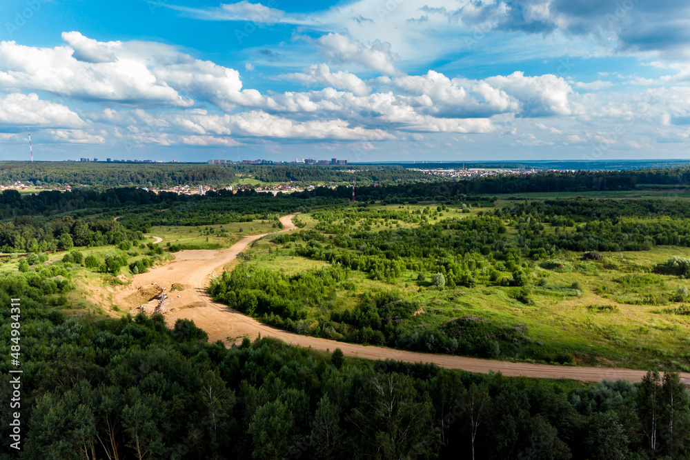 Obraz premium Panoramic view from a height of a country road in the middle of the countryside. Country and city buildings in the background