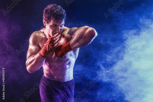 Portrait of muscular kickboxer who delivering elbow hit isolated on smoke background. Mixed media