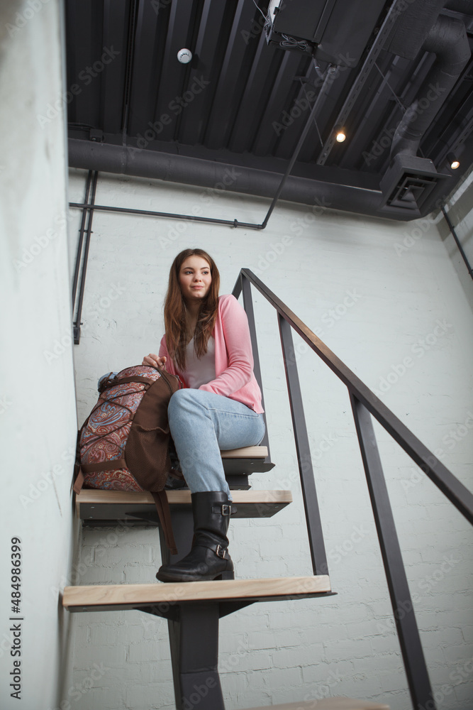 Vertical low angle shot of a beautiful female tourist with a backpack sitting on top of staircase at the hotel room
