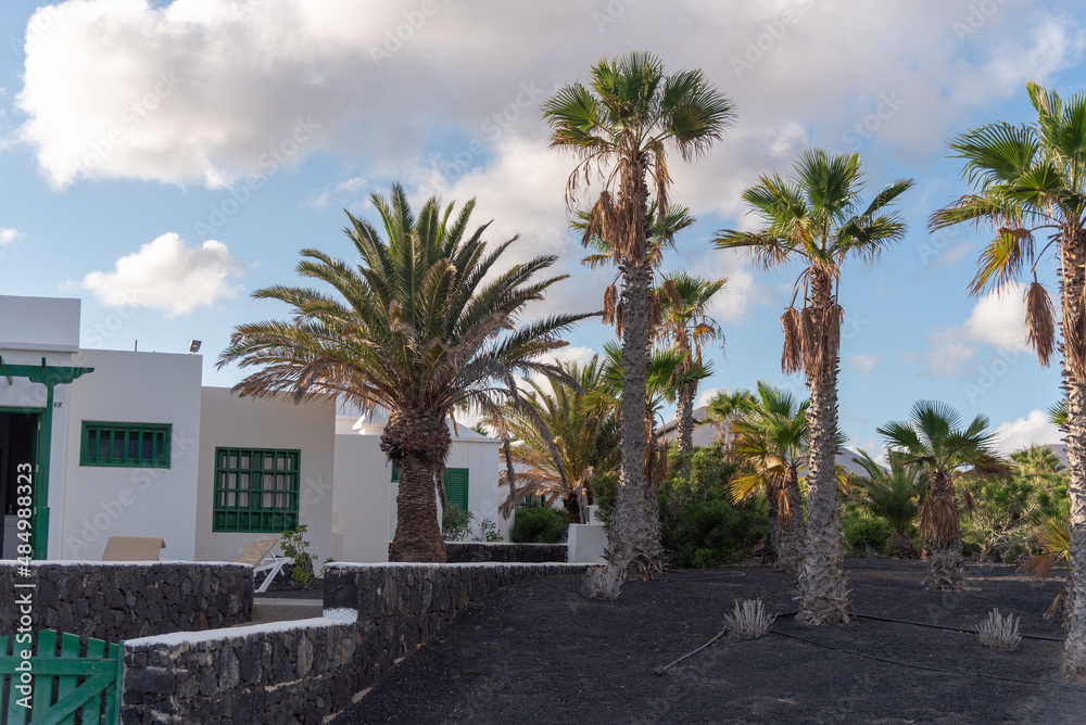 Casa tradicional de Lanzarote en Islas Canarias con la fachada blanca y rodeada por palmeras en un día de verano soleado pero con alguna nube