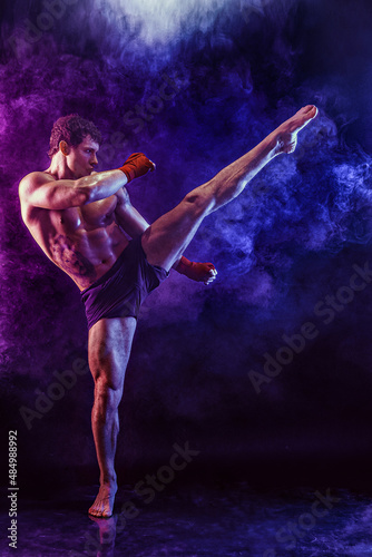 Full size of muay thai fighter who delivering leg kick to the head on smoke background. mixed media 