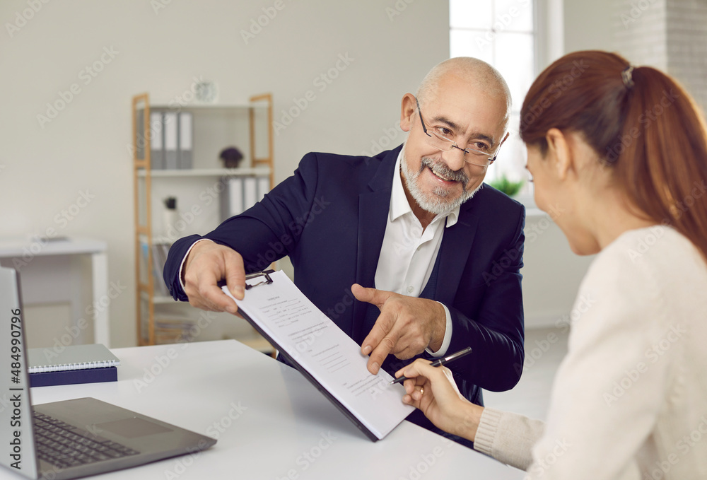 Obraz premium Happy woman puts signature on contract at bank or estate agency. Smiling loan broker, real estate agent or financial consultant sitting at office desk and giving agreement to young lady to sign