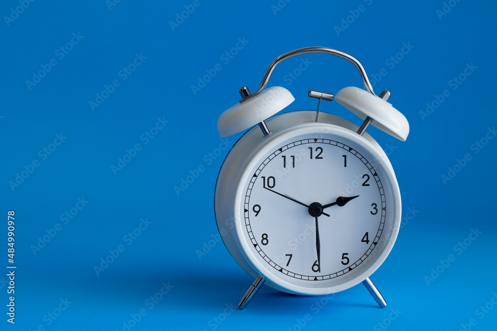 Isolated white alarm clock on a vibrant blue background with copy space Isolated white alarm clock on a vibrant blue background with copy space