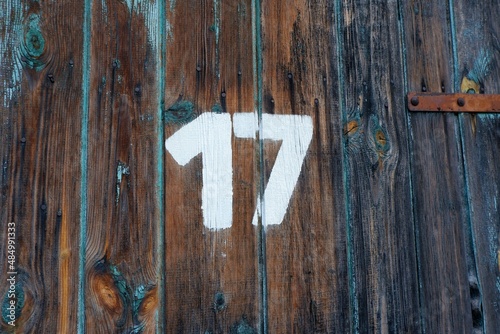 White colour number seventeen on an old abandoned weathered painted natural brown wooden gate of an old garage in Budapest suburb, Hungary