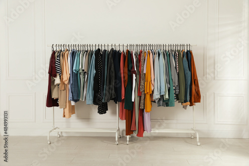 Racks with stylish clothes near white wall indoors. Fast fashion