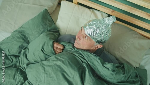 An Alarmed Man in a Foil Cap Suffering from Depression and Paranoia Suddenly Wakes Up In Bed. Insomnia, Nightmares, Panic. The Concept of Psychology, Loneliness, Fear and Mental Health. photo