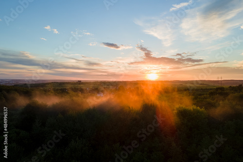 Aerial view of light fog covering dark forest trees at warm sunset
