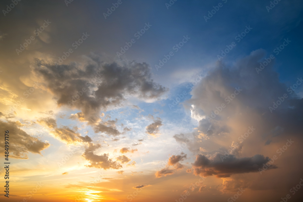 Dramatic sunset sky landscape with puffy clouds lit by orange setting sun and blue heavens
