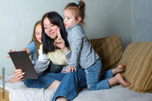 Three sisters have fun together at home on the couch, chat and browse something online on a tablet, mutual understanding and friendship between relatives in the family.