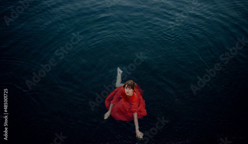 woman in wet red dress in dark blue water general shot from above