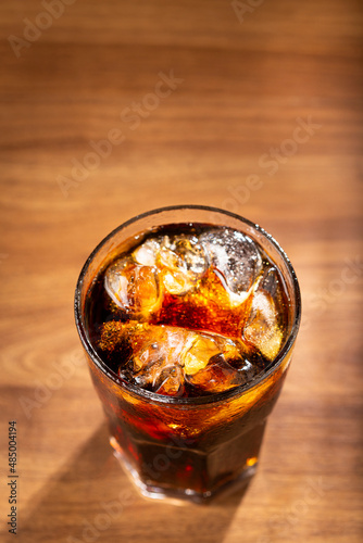 Coke glass with ice cubes on wooden table.