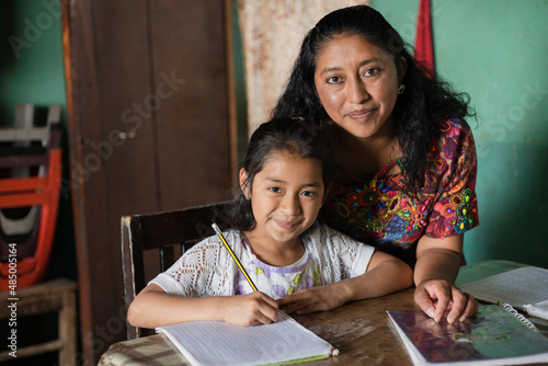 Hispanic mom helping her little daughter do her homework - Mom teaching her daughter to read and write at home - Mayan family at home photo