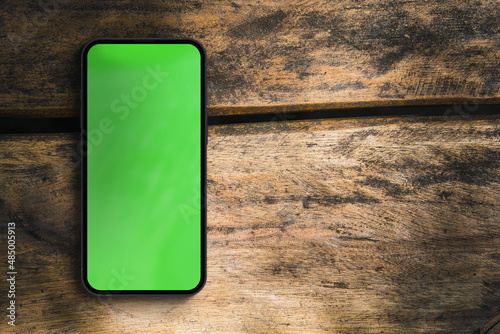 Fotografie Green screen on the smartphone screen on the rustic wooden table in the park