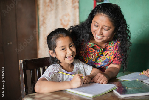 Hispanic mom helping her little daughter do her homework - Mom teaching her daughter to read and write at home - Mayan family at home