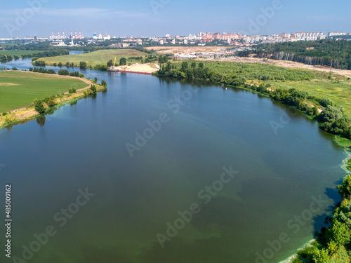 Large green field and trees near tranquil river in spring